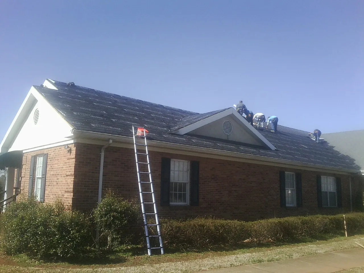 Crew tearing shingles off a brick ranch roof with a ladder set — Metal Roof Repair work by our crew in Hallsboro