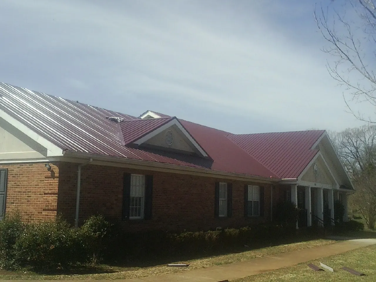 Red metal roof with gabled entries on a long brick building, from a Hail Damage Roof Repair job in Hallsboro