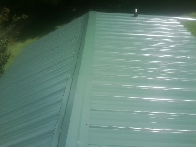 New green metal panels meeting at the ridge of a roof — Flat Roof Repair work by our crew in Hallsboro