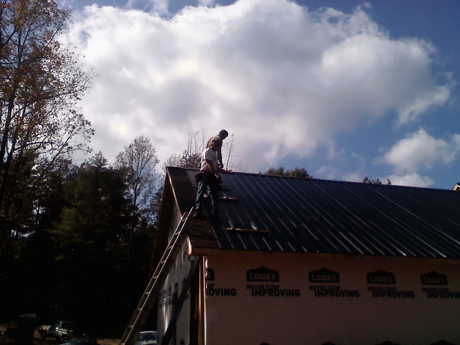 Roofer fastening dark metal panels high against a cloudy sky, from a Roof Inspection job in Hallsboro