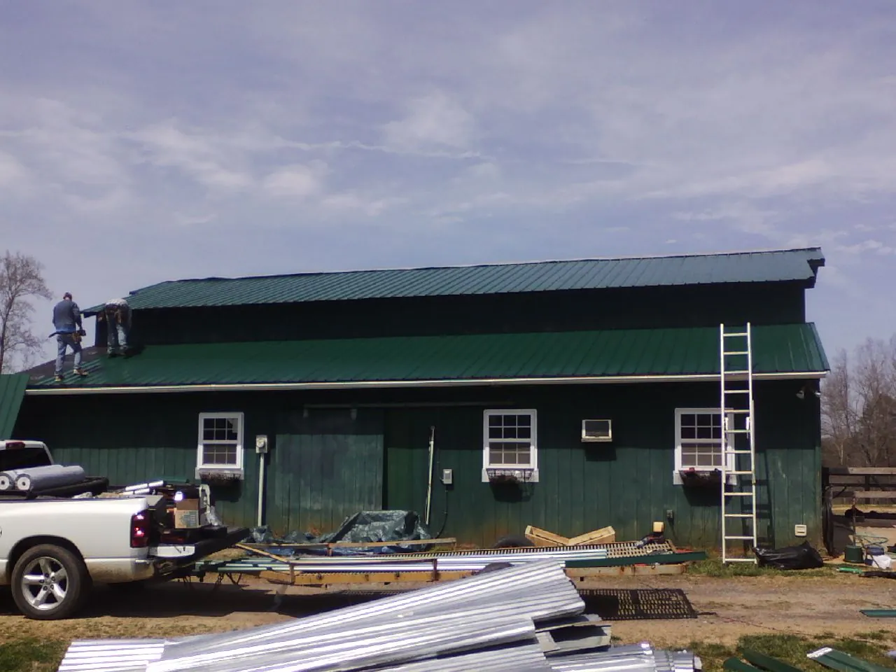 Crew installing green metal roofing on a large green barn in Hallsboro