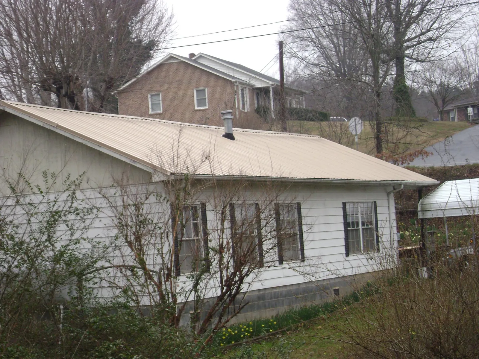 Tan metal roof on a white sided house set into a hillside — Commercial Roofing by Roofing Brothers in Hallsboro