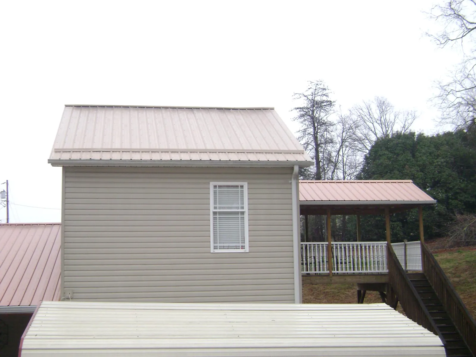 Tan metal roofs on a two story addition and attached porch, from a Roof Replacement job in Hallsboro